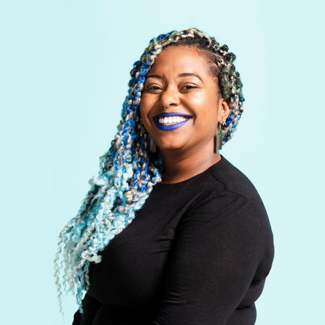 A woman of color with dark blue lipstick and braided blue colored hair smiling